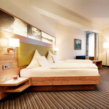 Im hellen Landhausstil eingerichtetes Hotelzimmer mit Doppelbett, Teppichboden, Sitzgelegenheit sowie Schreibtisch.
