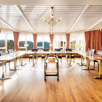 In a light-flooded room with a view of the Black Forest, there are U-shaped tables and chairs.