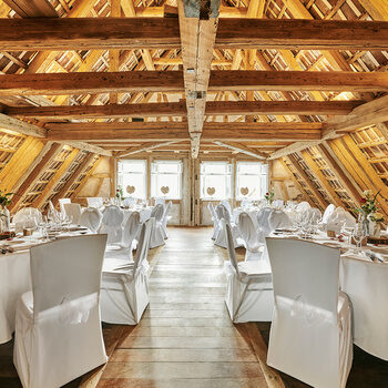 Ein feierlich bestuhlter Dachstuhl mit festlich eingedeckten, runden Tische und, mit weißen Hussen überzogenen, Stühlen.