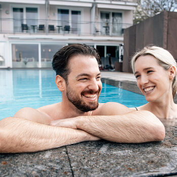 Ein gut gelauntes Paar entspannt zusammen in einem  Aussenpool des Wellnesshotels Berlins KroneLamm