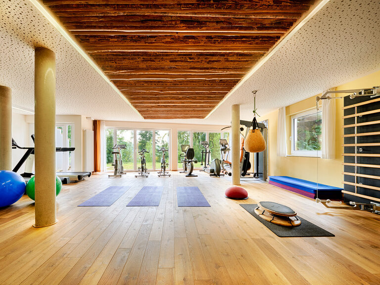 Ein Fitnessraum, der mit vielen verschiedenen Fitnessgeräten und Sportmatten ausgestattet ist.