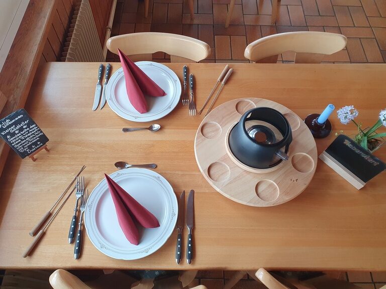 Ein eingedeckter Tisch mit Tellern, Besteck und Fonduetopf.
