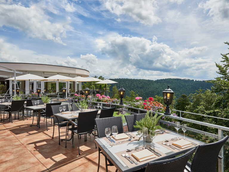 Eingedeckte Tische auf einer Terrasse mit Blick in den Schwarzwald.