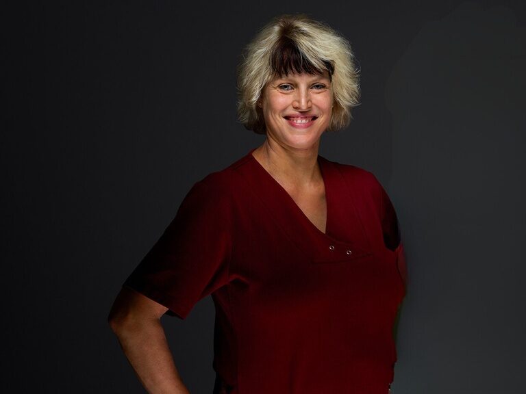 Physiotherapeutin Vanessa Berlin lächelt bei einem Portraitfoto vor dunklem Hintergrund.