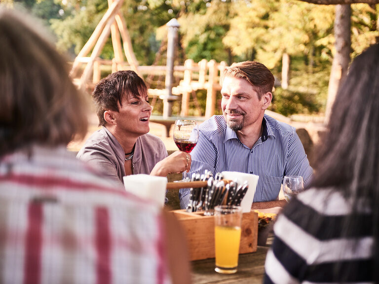 Vier Freunde sitzen gemeinsam mit Getränken an einem großen Tisch im Biergarten des Wanderheims.