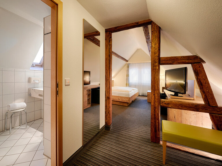 Ein Hotelzimmer mit Doppelbett, Schreibtisch, Fernseher, Sitzgelegenheit und modernem Badezimmer.