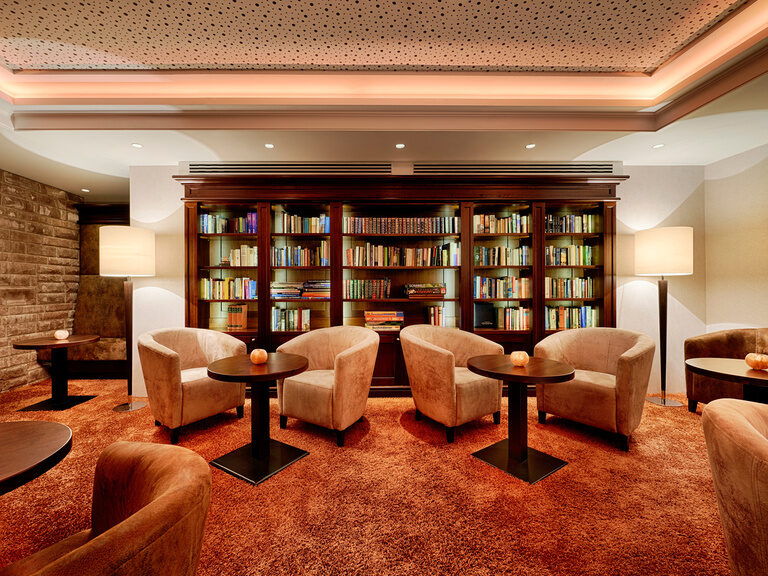 Cozy armchairs with tables on an orange carpet in front of a spacious bookcase.