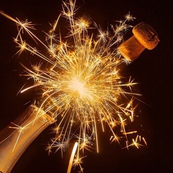 Zwischen dem Hals einer Champagnerflasche und deren Korken erleuchtet ein Feuerwerk.