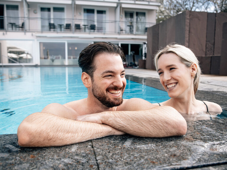A cheerful couple relaxes together in an outdoor pool at the Berlin KroneLamm wellness hotel