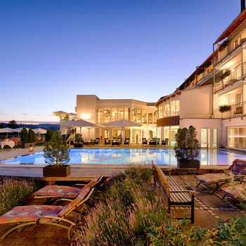 large, blue outdoor pool with numerous loungers in a romantic sunset setting.