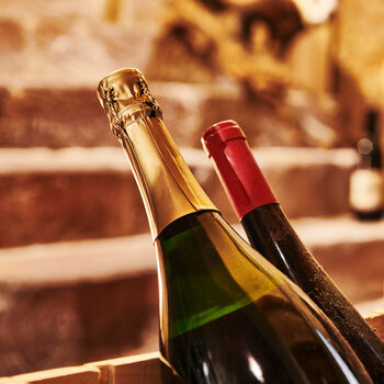Eine Flasche Champagner und eine Flasche Wein ragen aus einer Holzkiste, die sich in einem Gewölbekeller befindet.