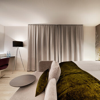 Ein modern ausgestattetes Hotelzimmer mit geschlossenen Vorhängen, das bei Nacht mit Lichtern romantisch beleuchtet wird.