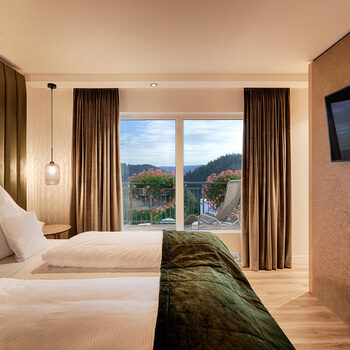 Ein komfortables Bett steht vor einem großen Panoramafenster, das die Idylle des Schwarzwalds zeigt.