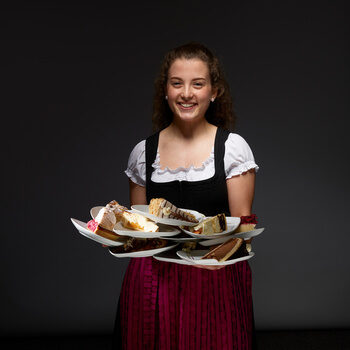 Eine junge Dame im Dirndl hält lächelnd Teller mit Kuchen in den Händen.