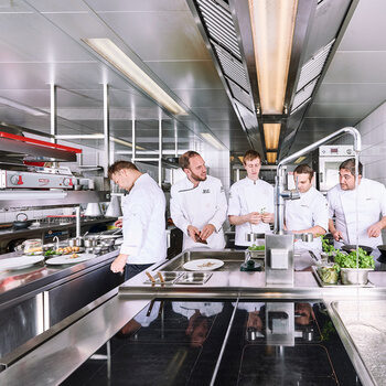 Fünf Köche arbeiten mit Freude in einer geräumigen Restaurantküche.