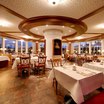 A large, round room with large panoramic windows, set tables and chairs.