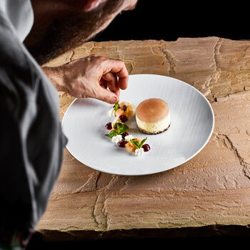 A chef garnishes a dessert on a white plate on a stone slab.
