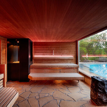 A red-lit sauna with a large panoramic window overlooking the hotel's outdoor pool.