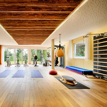 Ein Fitnessraum, der mit vielen verschiedenen Fitnessgeräten und Sportmatten ausgestattet ist.