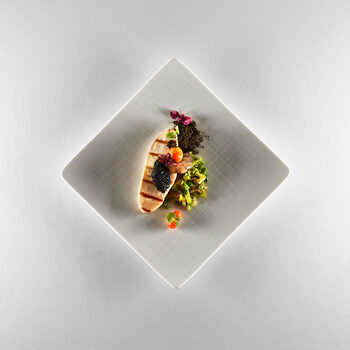 Ein quadratischer Teller auf dem hochwertiges Baguette, Kaviar, sowie eine Garnele exakt angerichtet wurden.
