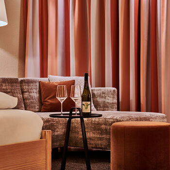 Zwei Weingläser stehen auf einem Tablet vor einer Couchsitzgruppe im Hotel KroneLamm