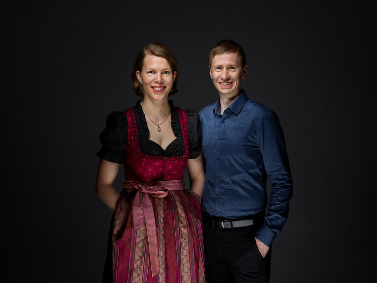 Elisabeth Röber-Berlin steht, in einem Dirndl gekleidet, neben Daniel Röber.