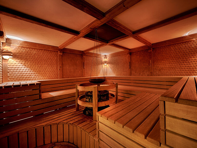 Holzbänke und ein Ofen für Aufgüsse in einer Sauna.