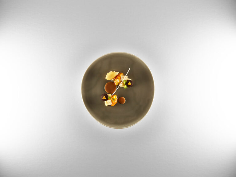 A dessert with chocolate and apricot in different variations on a dark gray plate.