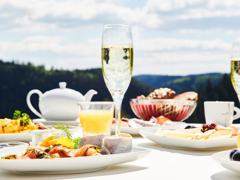 Ein reichlich gedeckter Frühstückstisch auf der Restaurantterrasse mit Blick auf den Schwarzwald im Hintergrund.