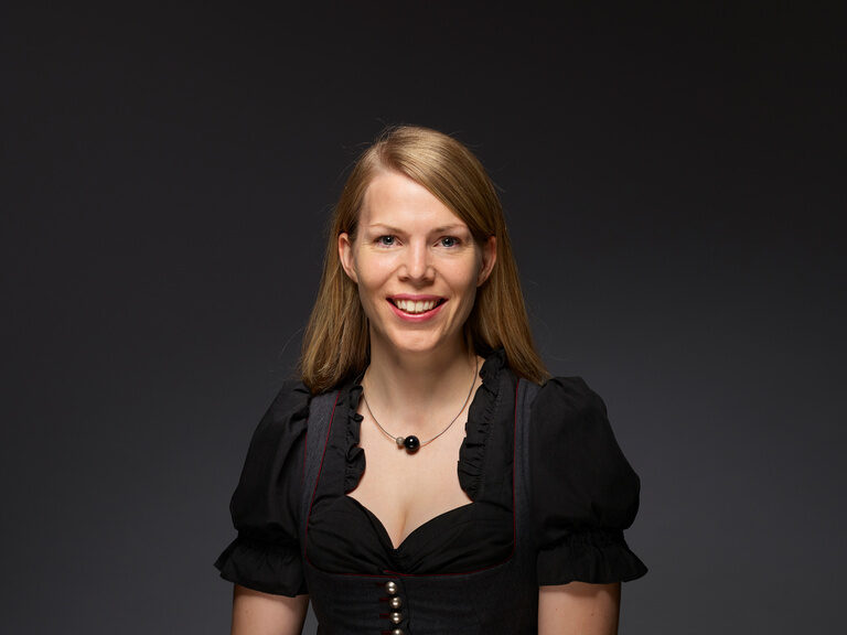 Elisabeth Röber-Berlin steht im Dirndl lächelnd vor einem dunklen Hintergrund.