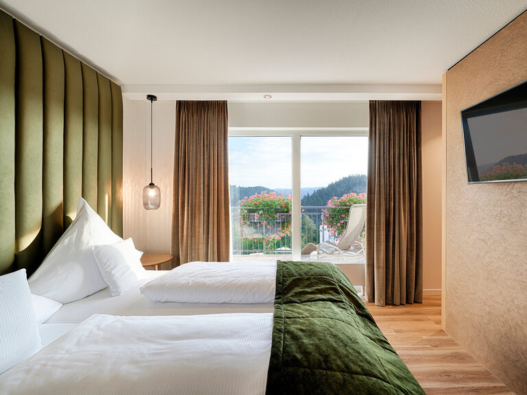 Cozy bed with a green bedspread in front of a large panoramic window.