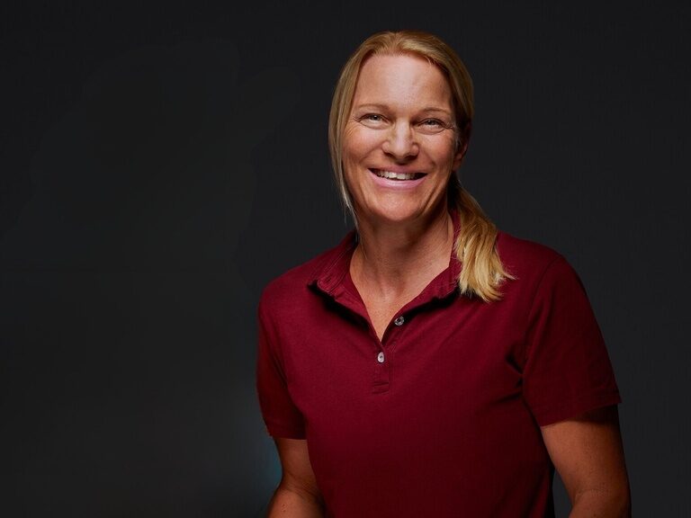 Sporttrainerin Kristina Möhrer lächelt bei einem Portraitfoto vor dunklem Hintergrund.