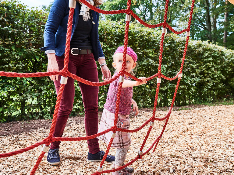Ein kleines Mädchen steht an einem roten Kletternetz Auf einem Spielplatz