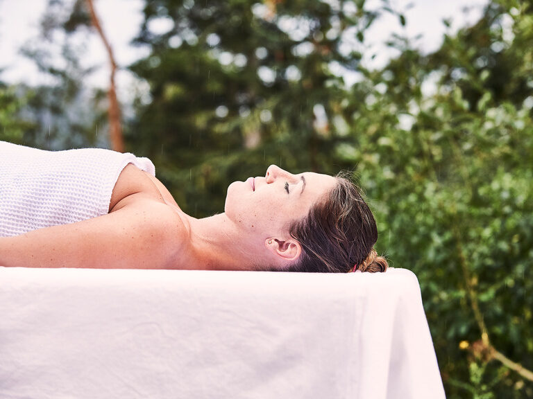 Eine junge Dame liegt entspannt auf einer Massageliege in der Natur.