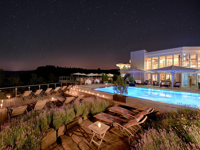 The hotel's outdoor pool shines in the darkness of the night and stars can be seen in the night sky.