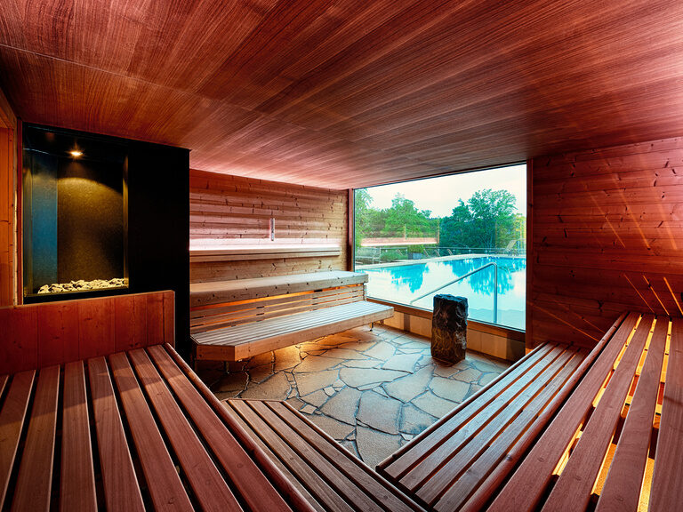 Red-lit sauna with wooden seating and large picture window overlooking the outdoor pool.