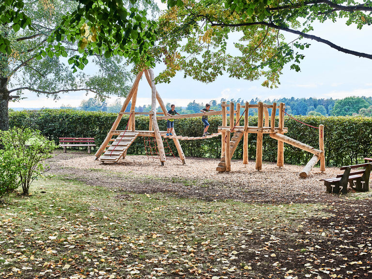 Two children walk across the bridge of the wooden playground in the beer garden of the hiking home.