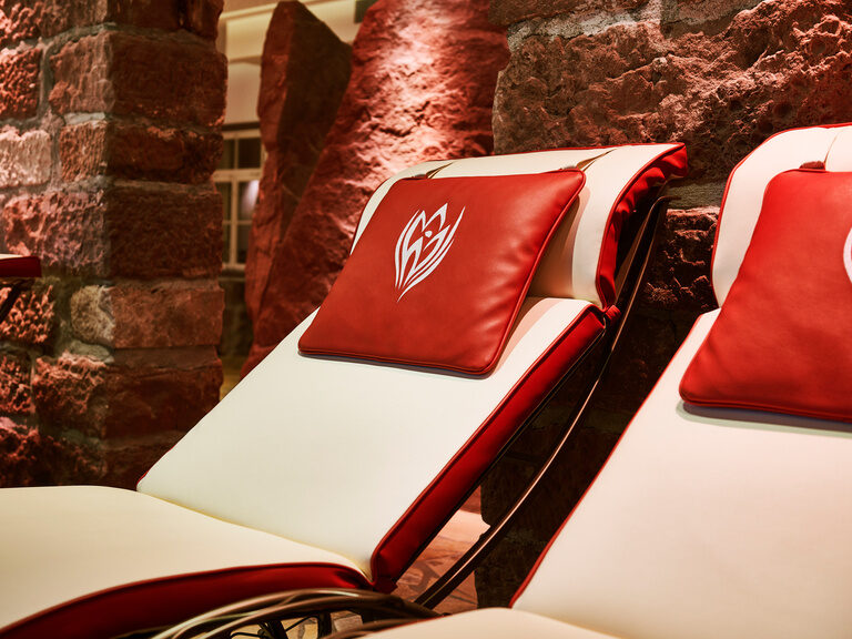 Close-up of spa loungers with beige cushions and a red pillow.