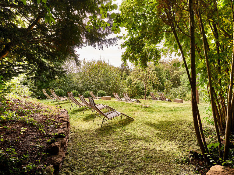Several loungers are lined up next to each other in the green garden of the Hotel Berlins KroneLamm.