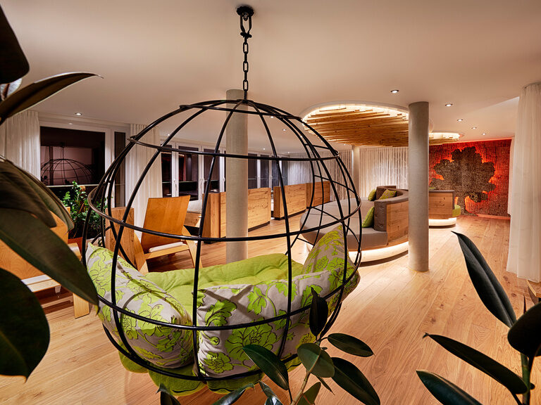 A large hanging chair with green cushions hangs in a large room with panoramic windows.