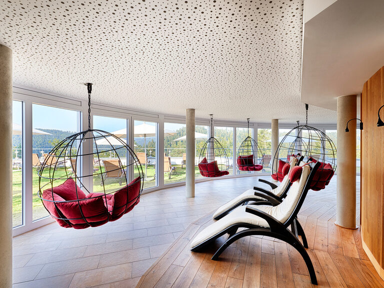 Hanging chairs with red cushions and loungers in a large relaxation room that offers a unique view of the Black Forest.