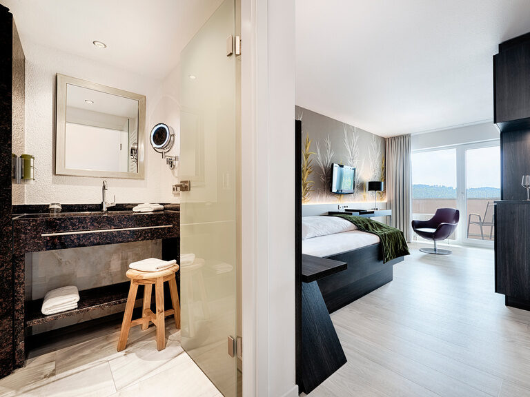 A modern sleeping and living area is separated by a wall from the attractively designed bathroom.