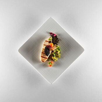 Ein quadratischer Teller auf dem hochwertiges Baguette, Kaviar, eine Garnele sowie feiner Salat und verschiedene Kressen und Kräuter exakt angerichtet wurden.