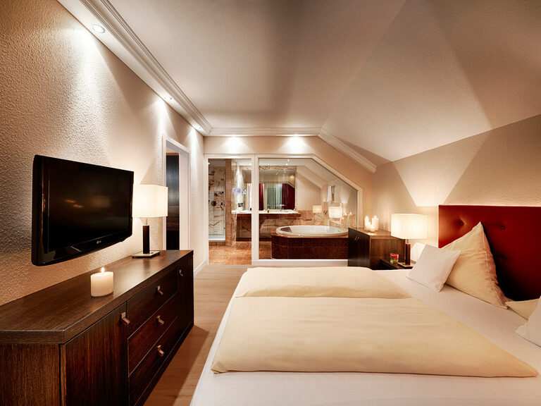 Ein großzügiges Zimmer mit gemütlichem Doppelbett, das an das Badezimmer mit Whirlpool angrenzt.