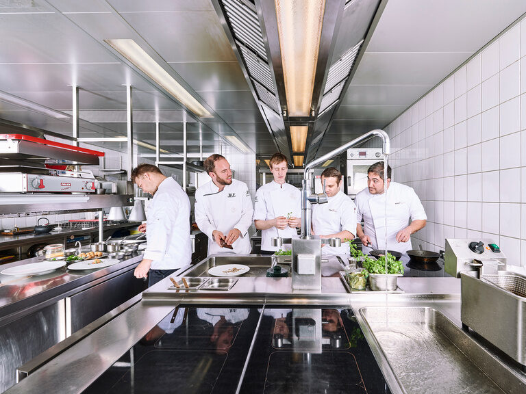 Fünf Köche arbeiten mit Freude in einer geräumigen Restaurantküche.