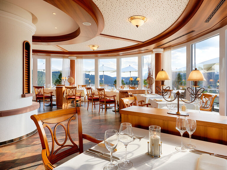 Ausschnitt eines Restaurants mit eingedeckten Tischen und Stühlen und einem traumhaftem Ausblick aus großen Panoramafenstern.