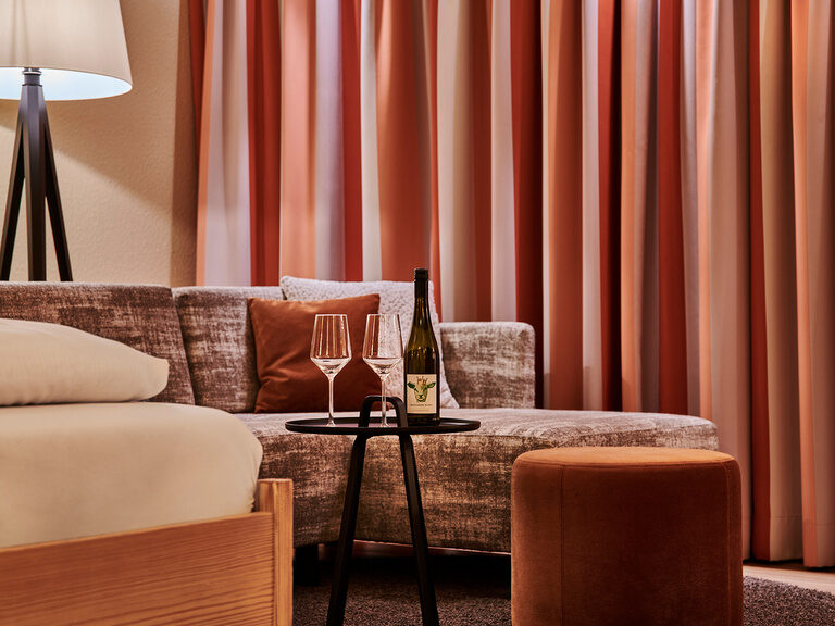 Zwei Weingläser stehen auf einem Tablet vor einer Couchsitzgruppe im Hotel KroneLamm