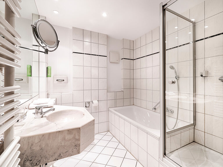Ein in weiß gehaltenes Badezimmer mit Dusche, Badewanne, Waschbecken, Toilette, Spiegel und Waschutensilien.