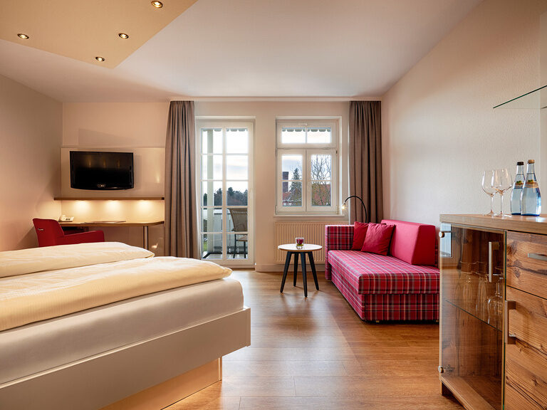 Modern eingerichtetes Doppelzimmer mit Holzboden, Doppelbett mit hohen Matratzen und komfortabler Sitzgelegenheit.