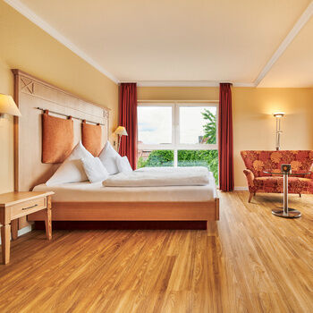 Ein geräumige Hotelzimmer mit Holzboden, gemütlichen Möbeln in warmen Farben und bequemem Doppelbett.